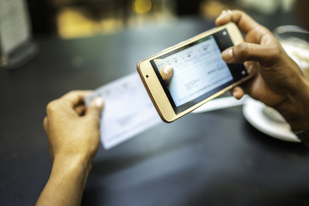 Young woman using mobile deposit to deposit check by phone in the cafe